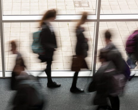 Blurred figures of school pupils walking past large windows in a corridor with tiled flooring