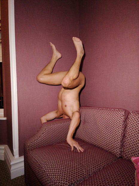 Naked man doing headstand on mauve sofa
