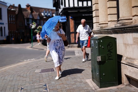 A woman holds an umbrella to protect herself from the sun as she walks along a street