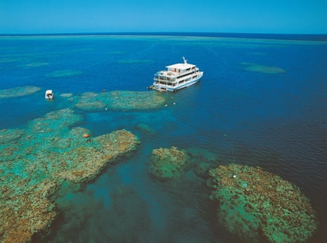 A white boat sits on the ocean above coral reef formations.