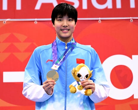 Yu Zidi holds a gold medal and plush mascot, smiling on the podium