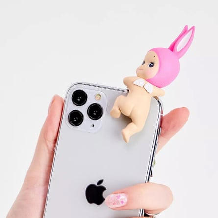 A baby with a pink bunny ears hood plastic figurine is clipped to the top of an iPhone