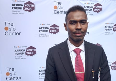 A young man in a suit and tie in front of a backdrop carrying the logos of the Oslo Foundation and Africa Youth Forum 2024