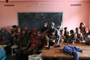 Older women and young children sit in a pink classroom