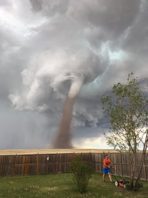 Theunis Wessels mows his lawn as a tornado blows behind him in Alberta, Canada on 2 June