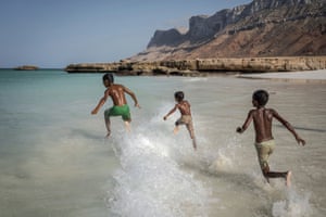 Three children run through the water near the shore