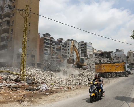 People ride a motorbike past ride past a destroyed building in Beirut’s southern suburbs