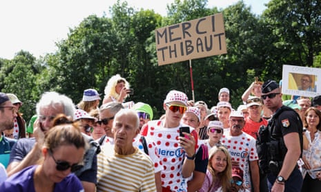 Spectators line the race route with a sign showing support for French rider Thibault Pinot.
