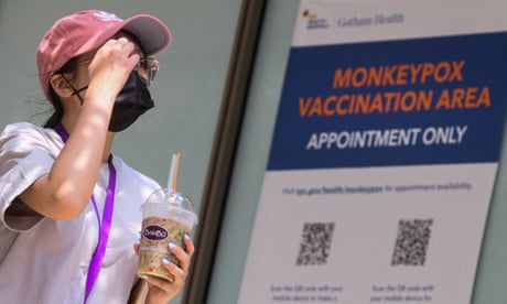 A woman wearing a red baseball cap and carrying a boba tea drink walks past a sign that reads 'Monkeypox vaccination area'.