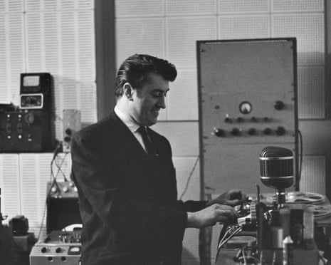 A monochrome image of Joe Meek working with a reel-to-reel tape recorder in his home recording studio.