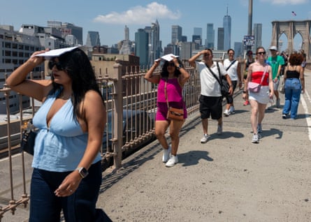 people shield their heads from the sun as they walk across a bridge