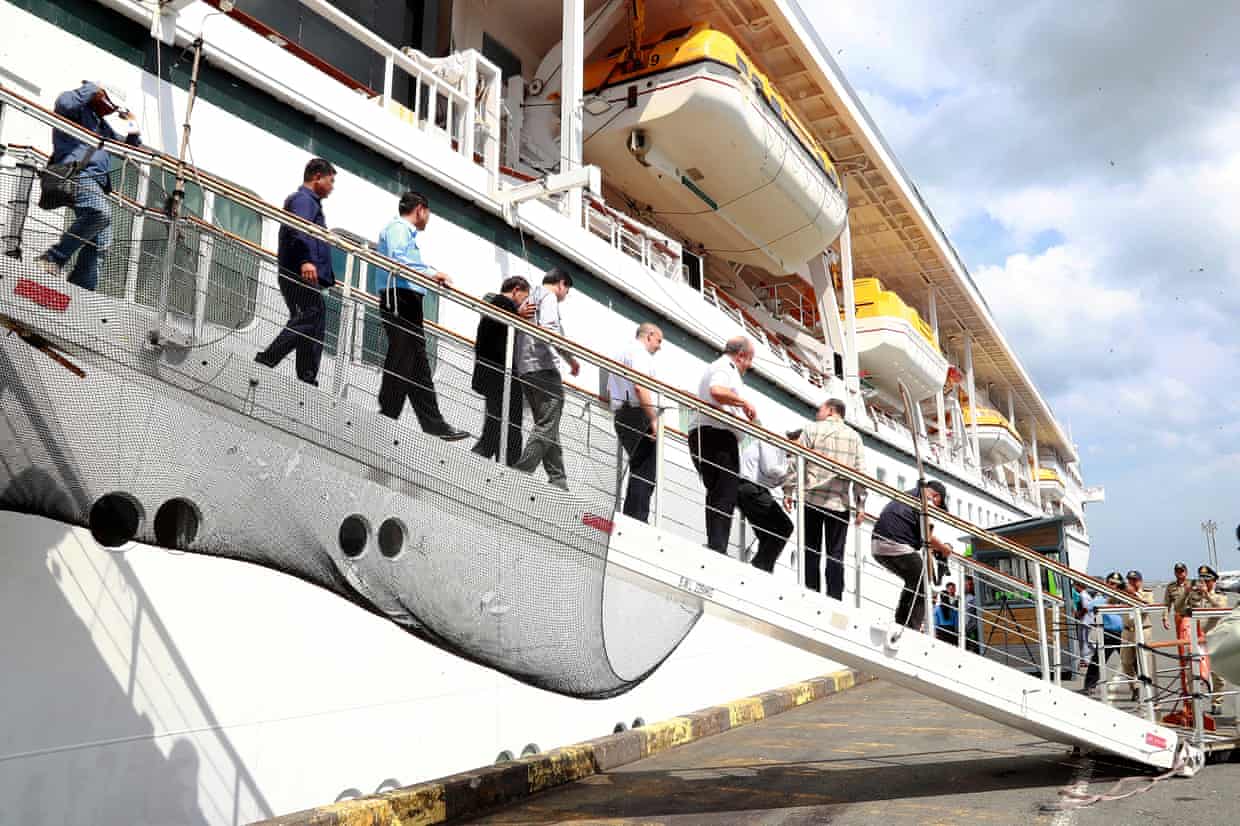 People, including a Cambodian minister, walk down a gangway from a docked cruise ship