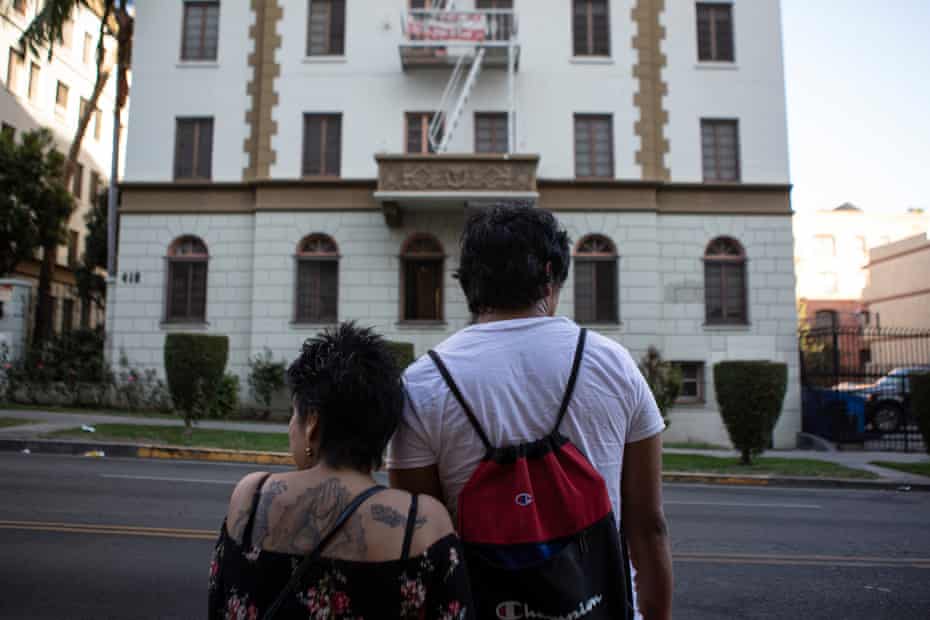 A man and a woman stand on the street facing a tall white apartment building