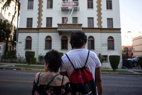 A man and a woman stand on the street facing a tall white apartment building