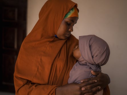 A Somali woman in an orange headscarf gently holds and gazes at her baby