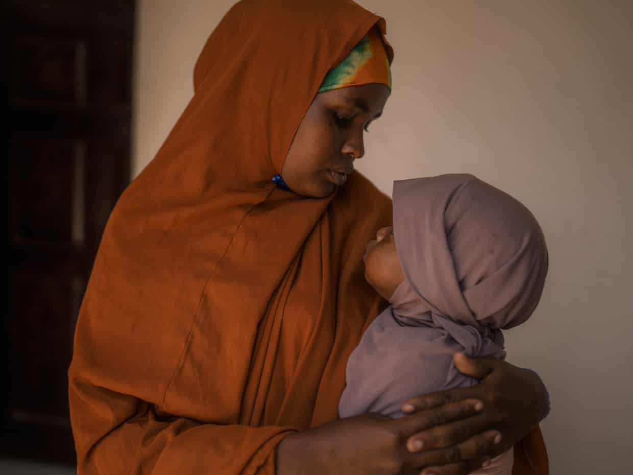 A Somali woman in an orange headscarf gently holds and gazes at her baby