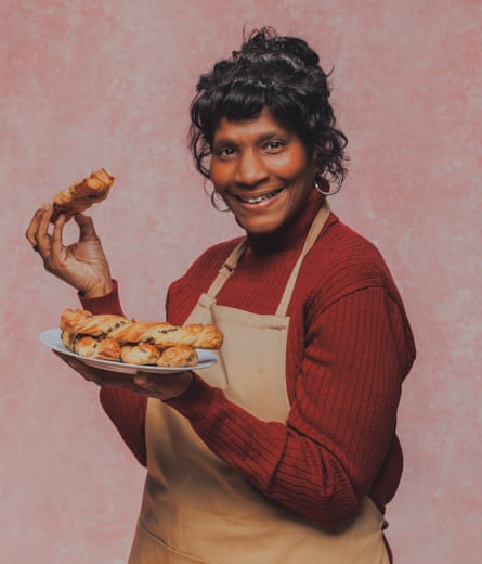 An older woman smiles and holds up a pastry.