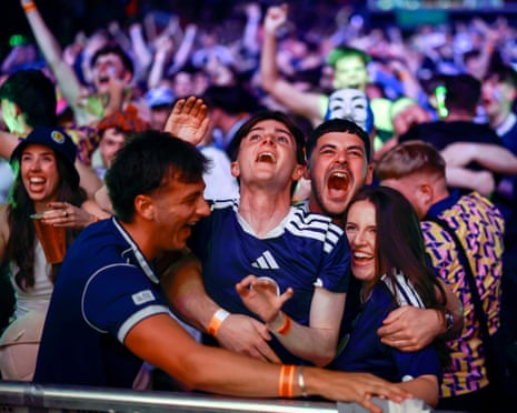 Four fans in Scotland shirts cheering and hugging each other at the barrier