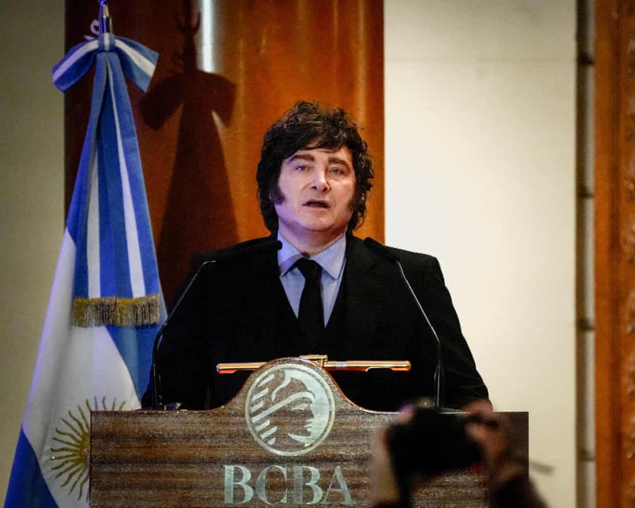 Javier Milei standing at a podium in front of an Argentinian flag