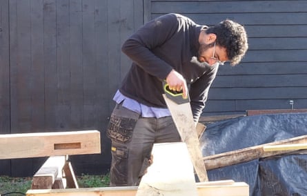 Saalim Elhaj saws a plank of wood on a workbench