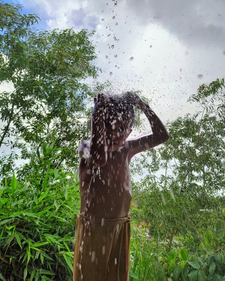 A Rohingya boy relishes the monsoon rain, dancing as he showers himself in the water cascading off a shelter.