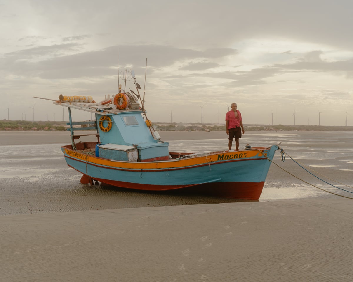 A man standing on the prow of a small fishing boat on a beach