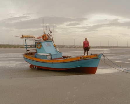 A man standing on the prow of a small fishing boat on a beach