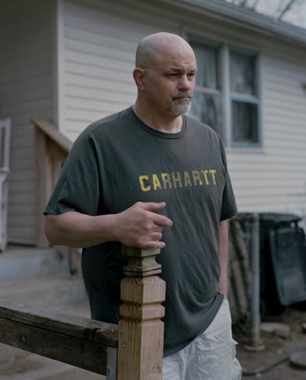 A man in a Carhartt T-shirt stands outside a home