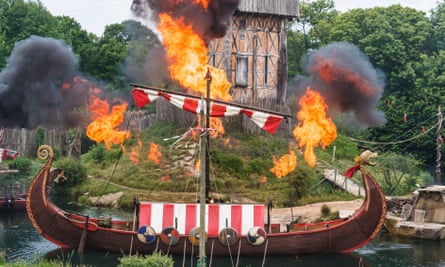 Smoke and flames leap around a model Viking long boat in a moat around a model medieval fort