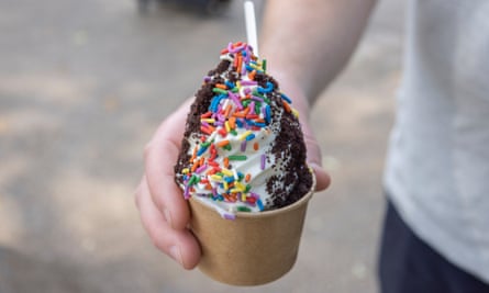 Close-up of a child’s hand holding whipped ice-cream with sauce and sprinkles