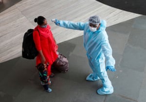 A health worker in personal protective equipment checks the temperature of a passenger at a train station in Mumbai.