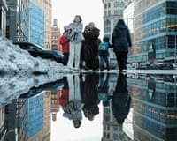 Pedestrians are reflected in a puddle of melting snow