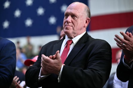 Man in suit claps in crowd, a large American flag covering wall behind him