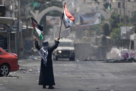 A Palestinian man waves Palestinian and Syrian flags in front of an Israeli army vehicle in Jenin’s refugee camp.