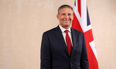 James Timpson, in a suit jacket, shirt and tie, grins broadly as he stands in front of a Union Jack flag in an official photo