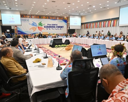 Delegates sit around a large rectangular table with screens positioned around the room
