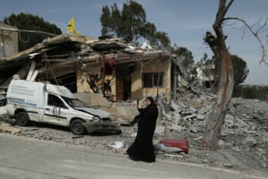 A woman stands in front of the destroyed house