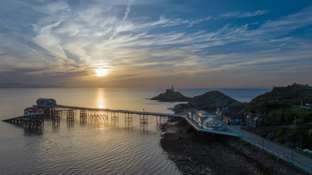 Sunrise over Mumbles lighthouse, pier and Beach Hut cafe in Swansea.