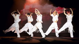 Five young men in white outfits dance on stage