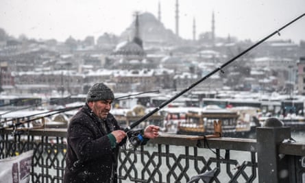 A man fishes on Galata bridge during snowfall in Istanbul.