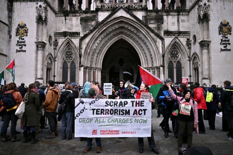 Over two dozen protesters outside court carrying a banner that says 'scrap the terrorism act, drop all charges now'.