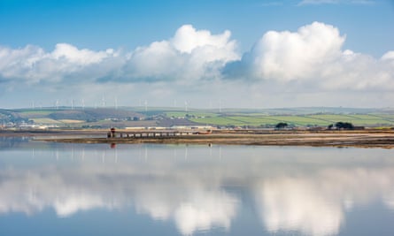 An expanse of water, with gently sloping hills in the distance and clouds reflected on the water