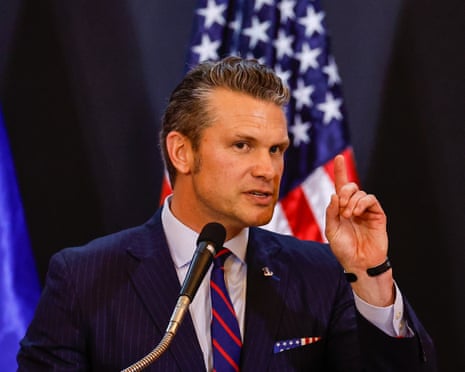 Pete Hegseth speaking from a podium with an American flag behind him