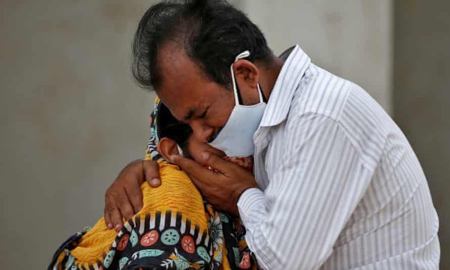 A weeping Indian man in a mask hugs an Indian woman