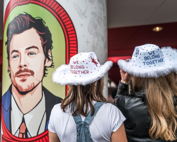 Harry Styles fans wearing cowboy hats in front of a poster of the singer