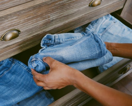Closeup of a black woman organising jeans in bottom drawer of dresser.