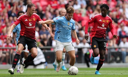 Manchester City’s James McAtee runs between Jonny Evans (left) and Kobbie Mainoo of Manchester United.