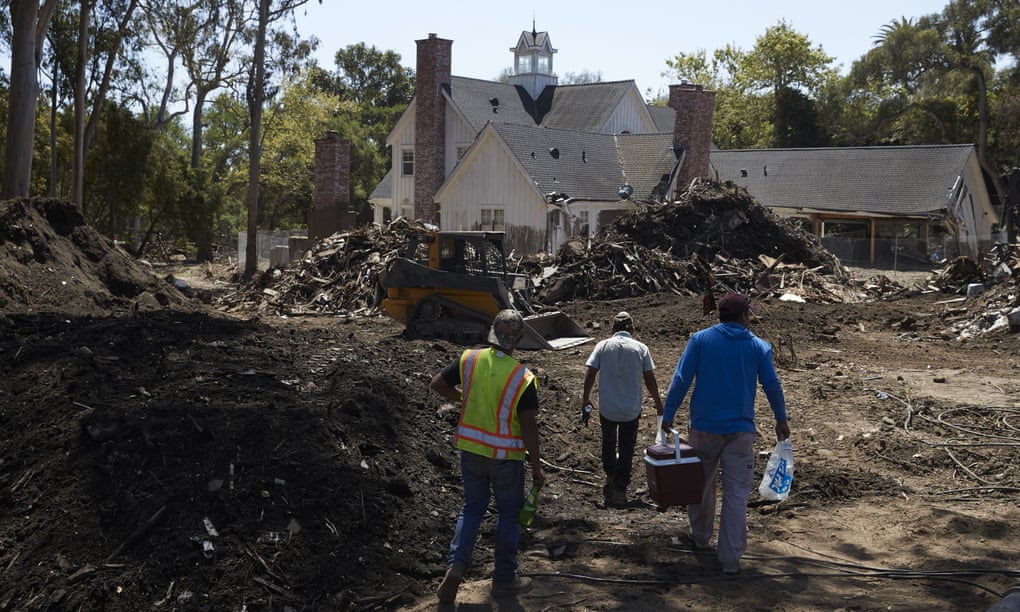 Workers walk past a pile of mud and debris outside a home heavily damaged by a mudslide in Montecito, California.