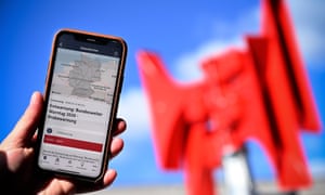 A smartphone displays the Nina app in front of the red horns of a warning siren in Leverkusen.