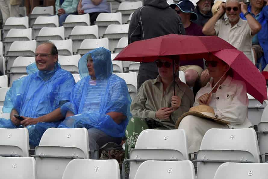 Spectators sit under umbrellas after rain stopped play on the first day of the third cricket test match between England and New Zealand at Headingley.